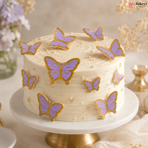 White cake with purple and gold butterfly decorations on a marble stand.