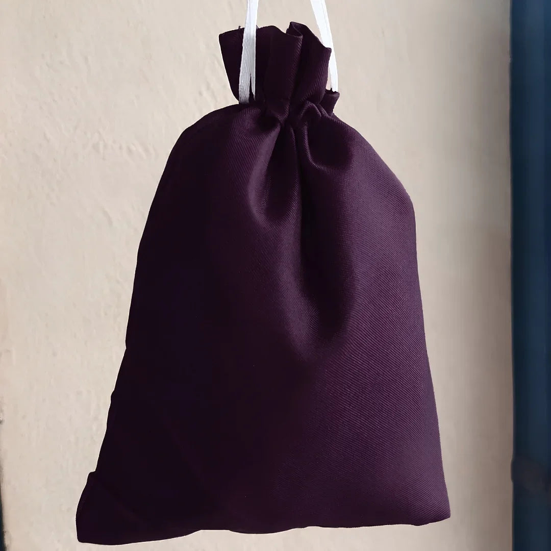 A dark purple drawstring pouch with white hanging strings, shown against a textured beige wall.