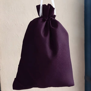 A dark purple drawstring pouch with white hanging strings, shown against a textured beige wall.