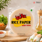 A 400g package of Yoka Rice Paper (Bânh Trâng) displayed on a wooden board with fresh spring rolls, vegetables, and a pepper mill in a kitchen setting.