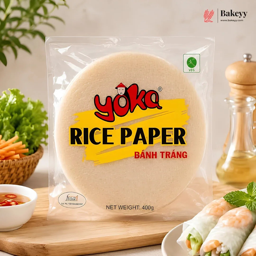 A 400g package of Yoka Rice Paper (Bânh Trâng) displayed on a wooden board with fresh spring rolls, vegetables, and a pepper mill in a kitchen setting.
