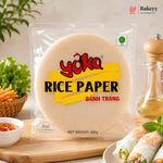 A 400g package of Yoka Rice Paper (Bânh Trâng) displayed on a wooden board with fresh spring rolls, vegetables, and a pepper mill in a kitchen setting.
