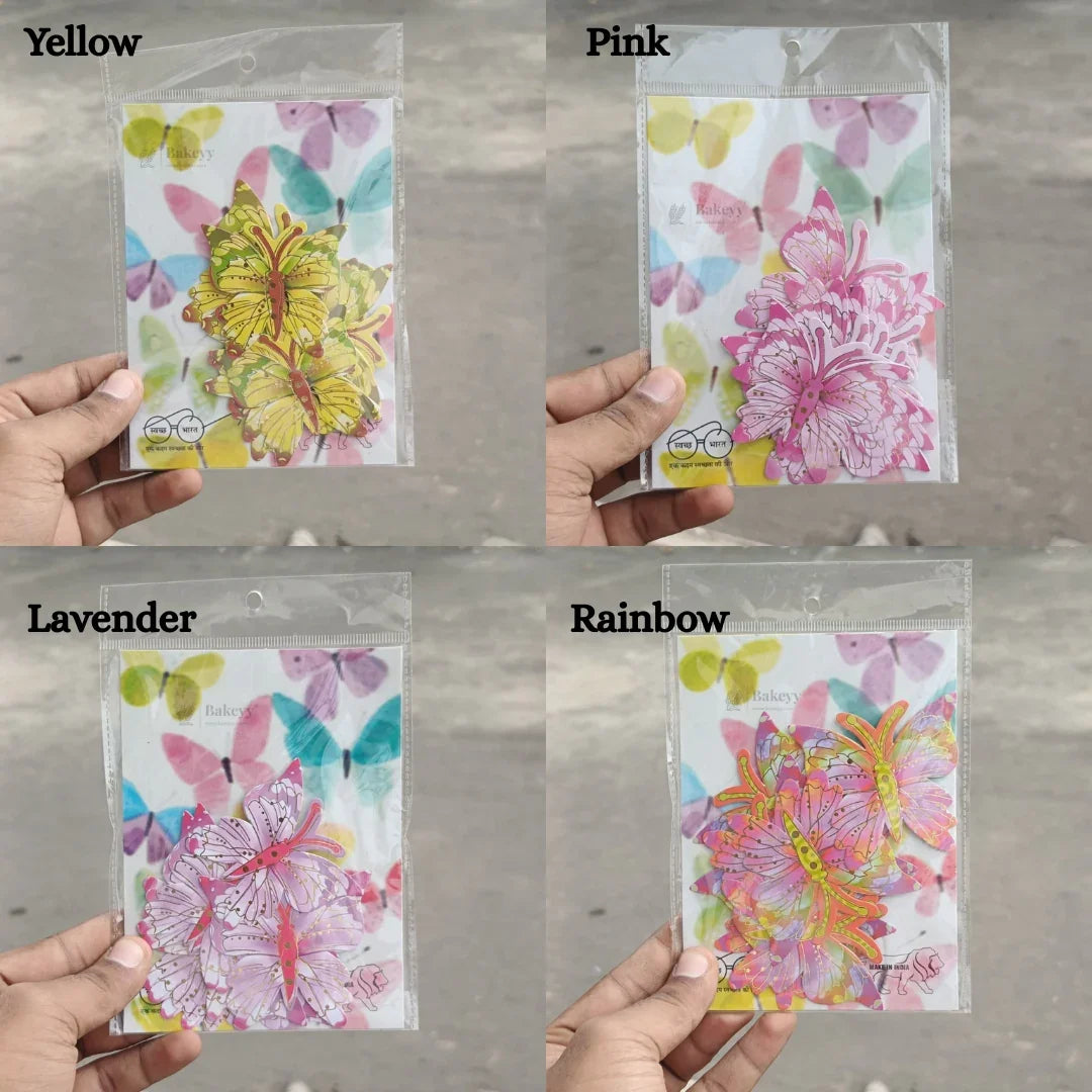 Hand holding four colorful butterfly toppers in yellow, pink, lavender, and rainbow variants, ideal for baking and gift packaging from Bakeyy.com.