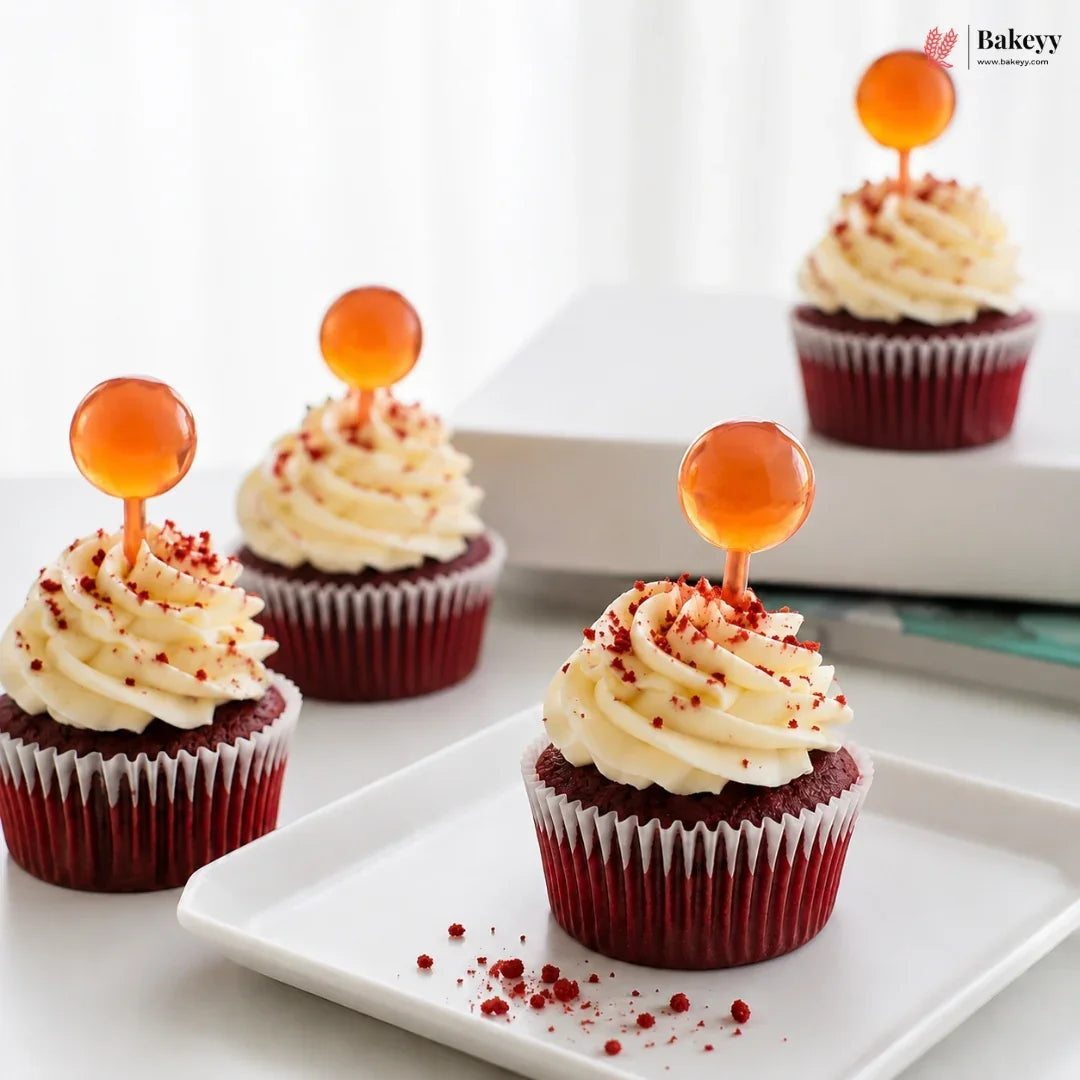 Red velvet cupcakes with cream cheese frosting and orange spherical decorations on a white plate.