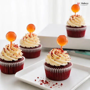 Red velvet cupcakes with cream cheese frosting and orange spherical decorations on a white plate.