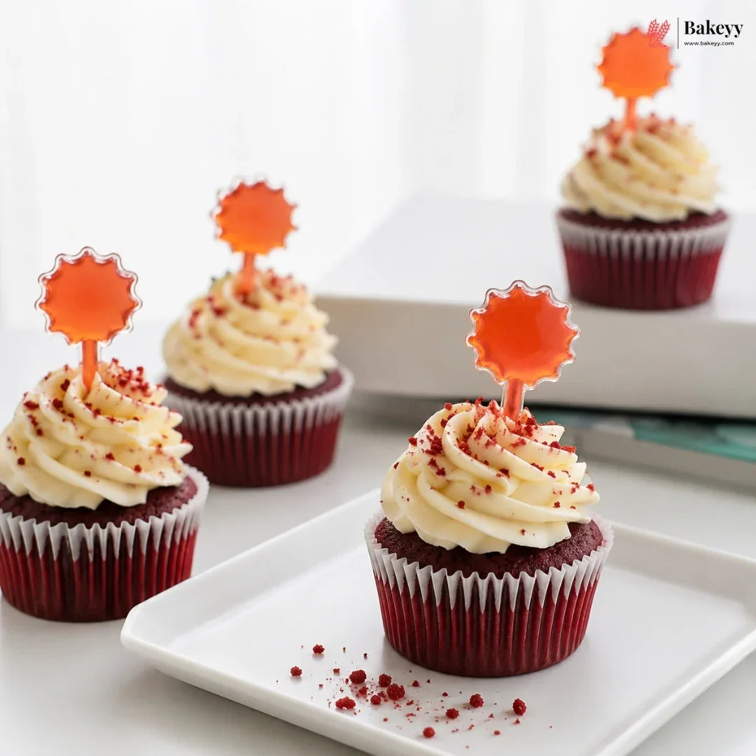 Red velvet cupcakes with cream cheese frosting and orange star-shaped toppers on a white plate.