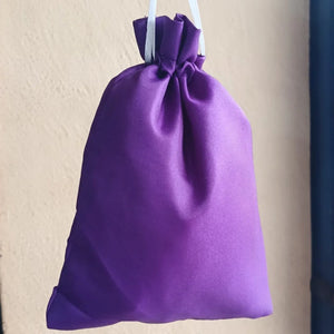 Purple drawstring bag hanging against a beige wall