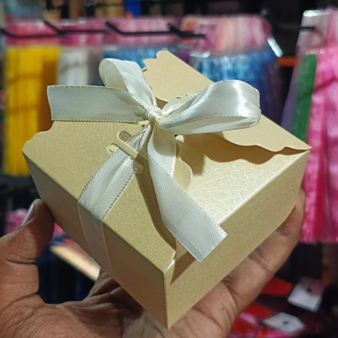 Beige gift box with a white ribbon held by a hand against a blurred background