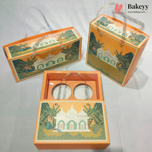 Three orange decorative gift boxes with illustrated temple and garden designs, shown on a light gray fabric background. One box is open, revealing two round white inserts, and the Bakeyy logo appears in the top right corner.