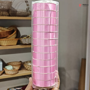 Roll of pink ribbon in clear packaging held in front of a shelf with wicker baskets.