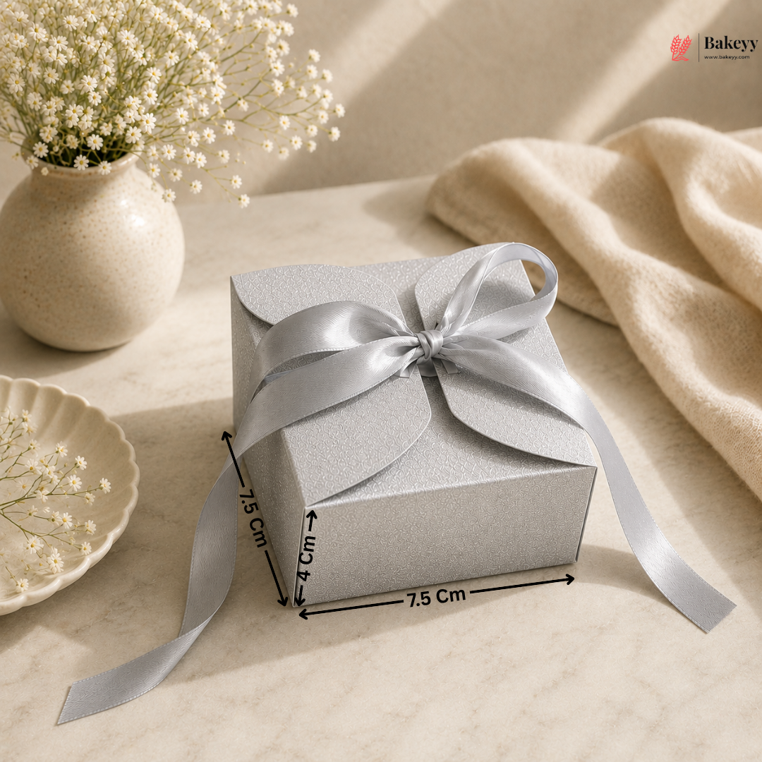 Silver gift box with a bow on a beige surface with flowers and a vase.