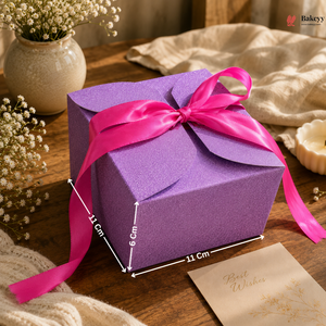 Purple gift box with a pink ribbon on a wooden surface with decorative elements.