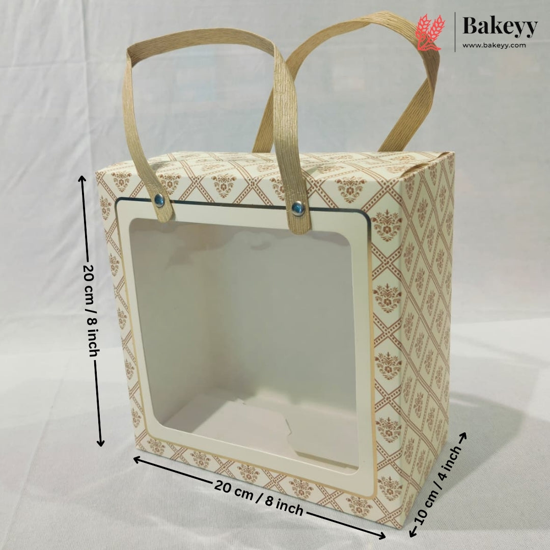 A rectangular bakery gift bag or display box with a clear front window and two tan handles, shown on a white backdrop with dimension arrows and labels indicating 20 cm by 20 cm by 10 cm.