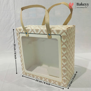 A rectangular bakery gift bag or display box with a clear front window and two tan handles, shown on a white backdrop with dimension arrows and labels indicating 20 cm by 20 cm by 10 cm.