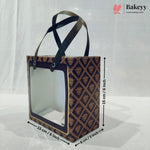 A rectangular bakery gift bag with a clear front window and dark handles, shown with dimension arrows and labels indicating 15 cm by 8 cm. The bag has a dark navy and gold geometric pattern.