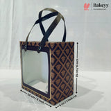 A rectangular bakery gift bag with a clear front window and dark handles, shown with dimension arrows and labels indicating 15 cm by 8 cm. The bag has a dark navy and gold geometric pattern.