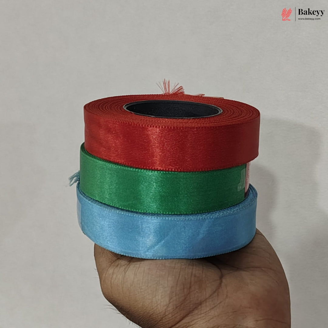 Three rolls of ribbon in red, green, and blue held by a hand against a plain background.