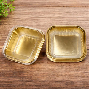 Gold square pastry packaging boxes with clear lids on wooden surface, Bakeyy baking supplies.
