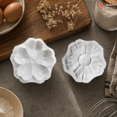 Two white decorative cookie cutters on a rustic kitchen counter with eggs and flour in the background.