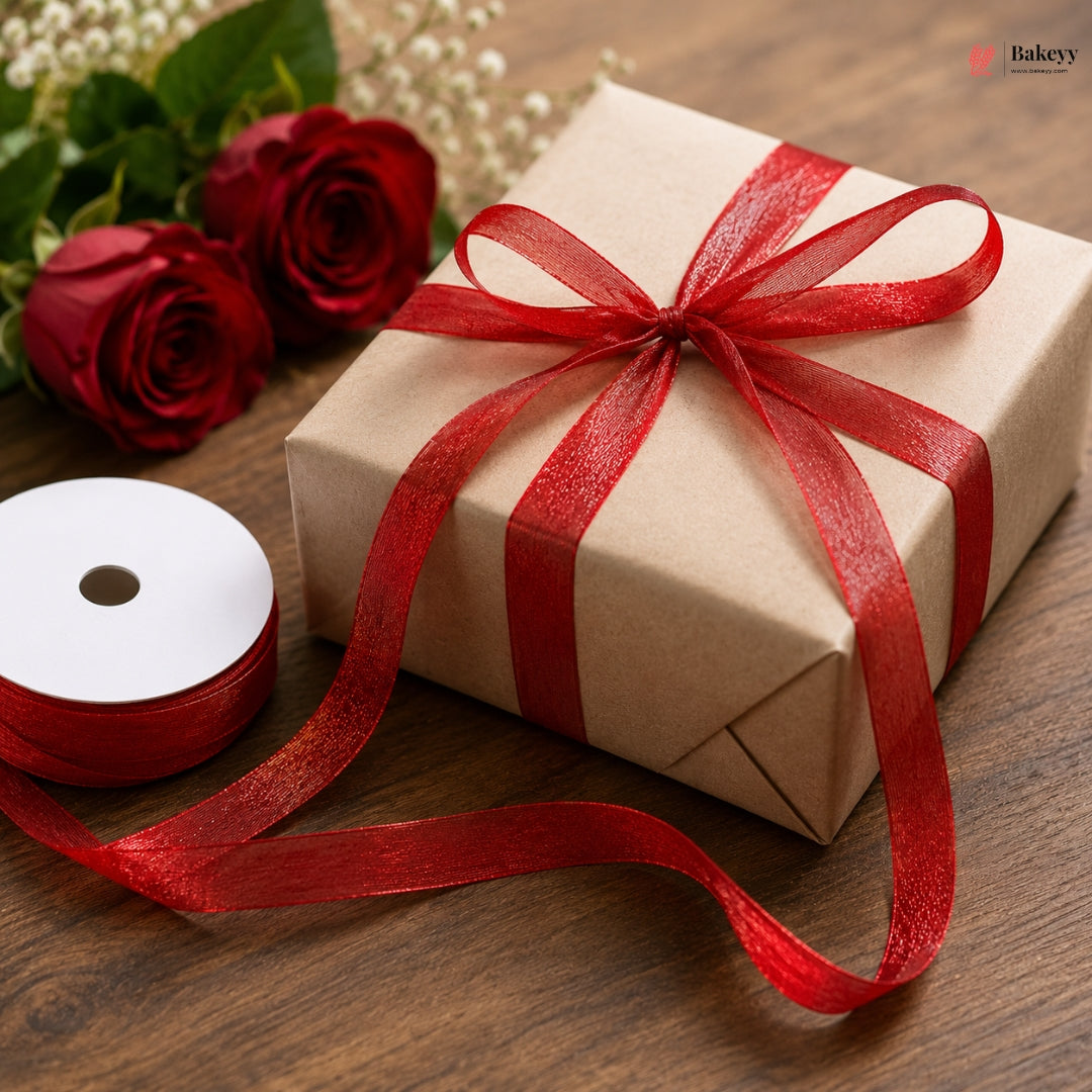 Gift box wrapped in brown paper with a red ribbon, accompanied by red roses and white flowers on a wooden surface.
