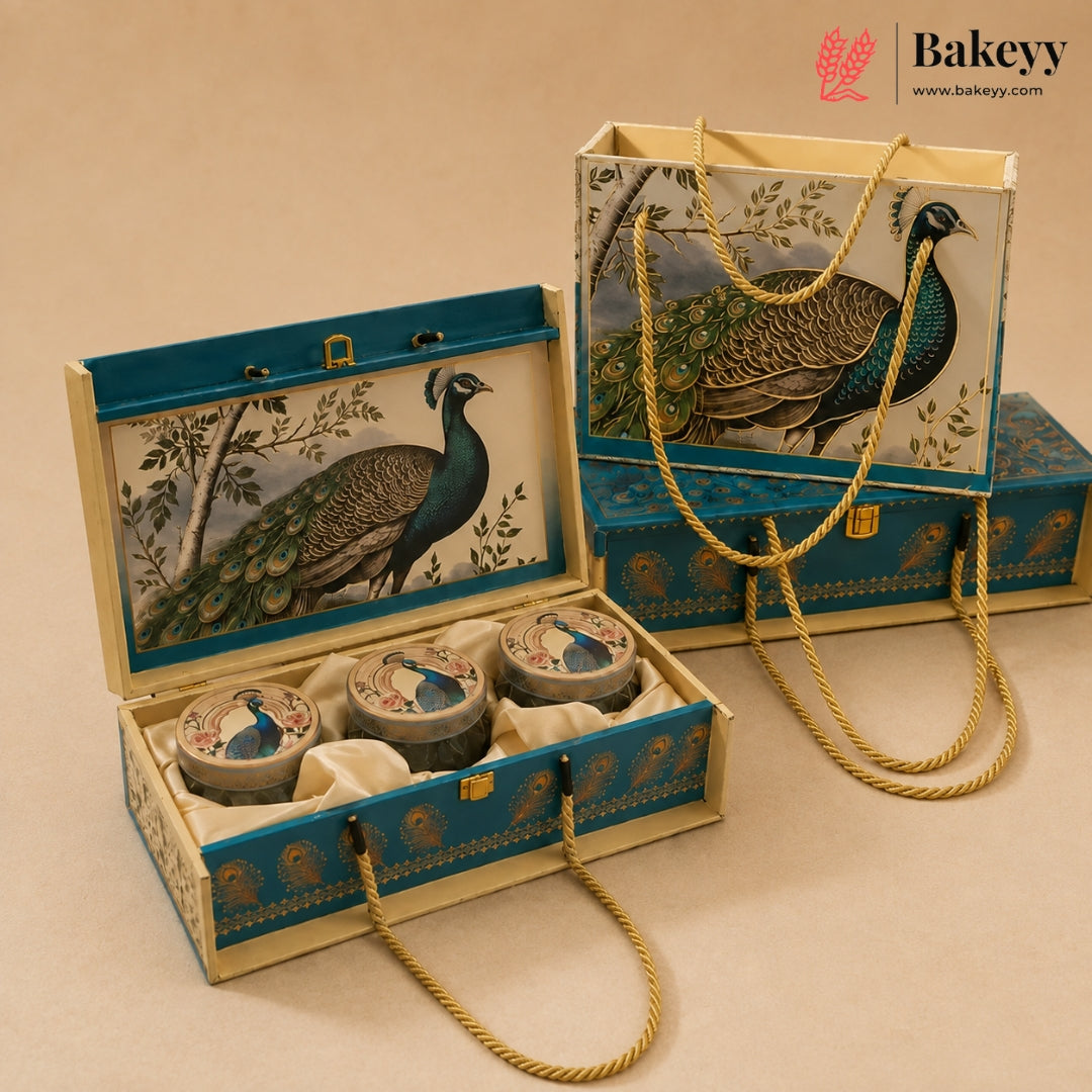 A decorative gift box set for baked goods, featuring an open rectangular box with three round tin containers inside, alongside a matching tote bag and closed box. The packaging is decorated with a detailed peacock illustration and blue-gold patterns on a cream background, with gold rope handles.