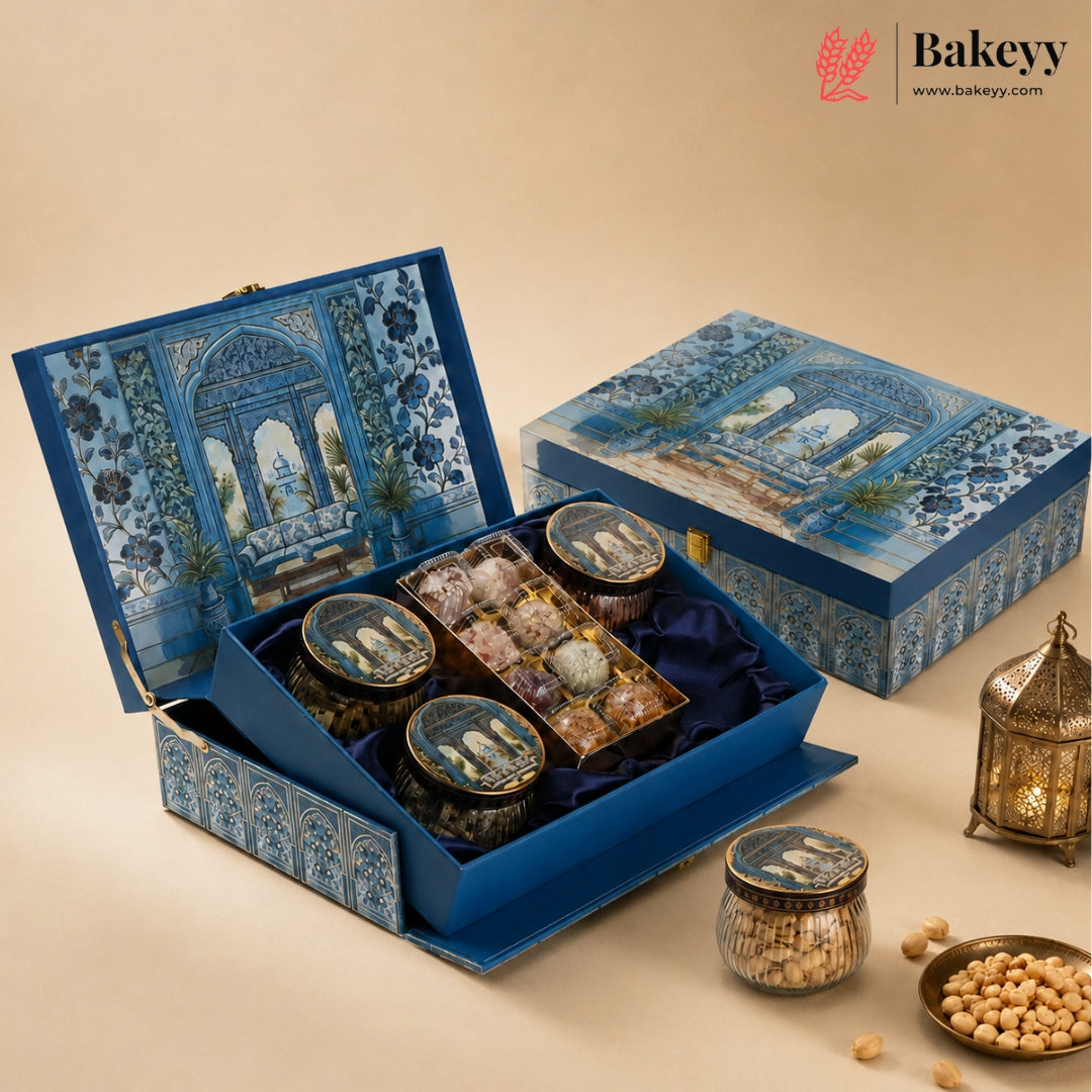 A luxury Bakeyy gift set featuring a blue patterned presentation box opened to reveal four glass jars of nuts and chocolates, with additional jars and decorative lanterns on a beige background.
