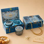 An ornate blue gift set box with gold detailing, shown open and closed on a beige background. The set includes decorative glass jars with blue lids, a blue satin lining, a gold rope handle, and a small card reading 'For Your Special Moments.