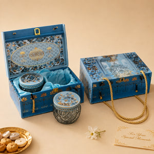 An ornate blue gift set box with gold detailing, shown open and closed on a beige background. The set includes decorative glass jars with blue lids, a blue satin lining, a gold rope handle, and a small card reading 'For Your Special Moments.