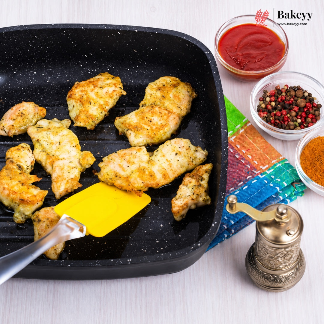 Grilled chicken breast strips cooking in a black grill pan with a yellow spatula, styled with small bowls of tomato sauce, peppercorns, and spices on a white surface. The Bakeey logo is visible in the top right corner.