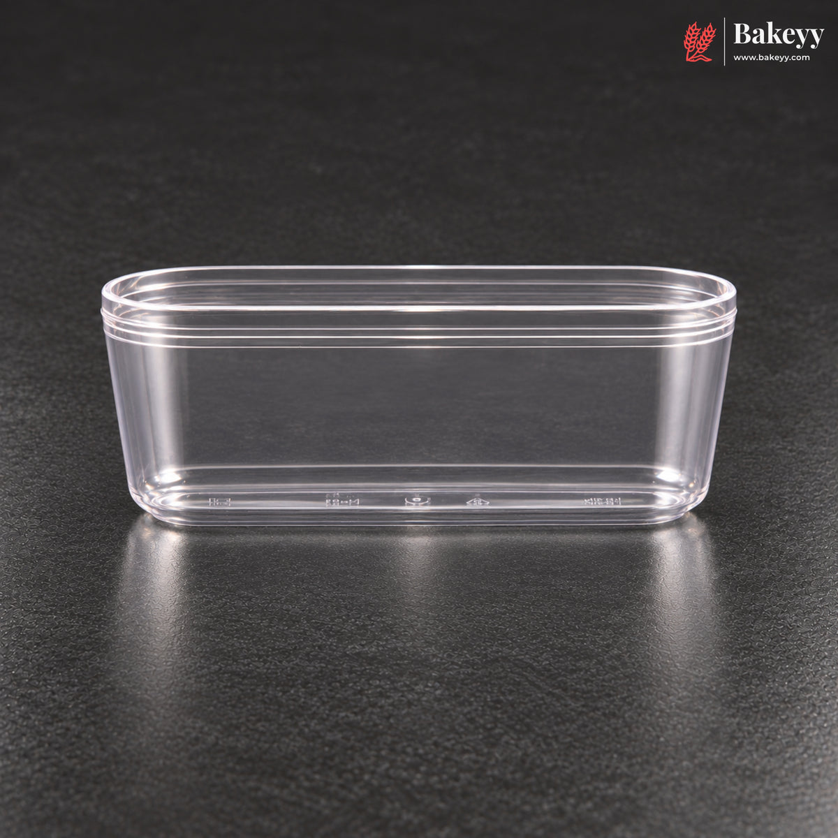 A clear plastic rectangular container with a flared rim, shown on a dark textured surface. The Bakeyy logo is visible in the top right corner.