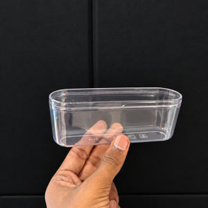 A hand holding a small, clear plastic rectangular container against a dark black background.