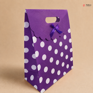 Purple gift bag with white polka dots and a purple ribbon on a beige background