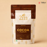 A 1kg stand-up pouch of 2m Brown Cocoa Powder, featuring a white and dark brown design with gold text and cocoa bean illustrations, set against a solid beige background.