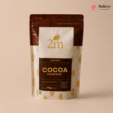 A 1kg stand-up pouch of 2m Brown Cocoa Powder, featuring a cream and dark brown design with gold cocoa bean illustrations, set against a solid beige background.