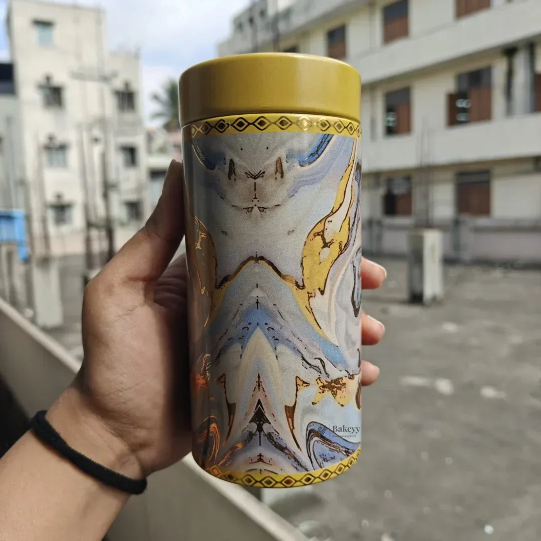 Hand holding decorative cylindrical container with gold lid and marbled design, Bakeyy packaging