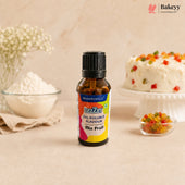 A bottle of Bakersville oil soluble flavouring mix, fruit flavour, standing on a beige surface with baking ingredients and a decorated cake blurred in the background.