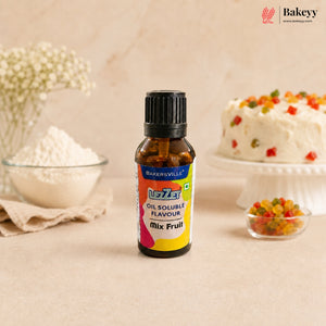 A bottle of Bakersville oil soluble flavouring mix, fruit flavour, standing on a beige surface with baking ingredients and a decorated cake blurred in the background.