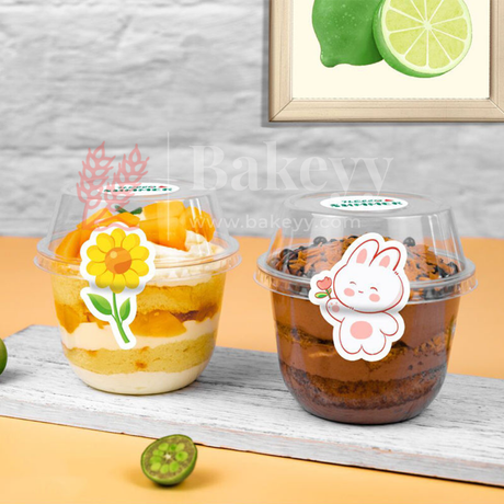 Two transparent dessert cups with colorful contents on a wooden surface, featuring decorative stickers.