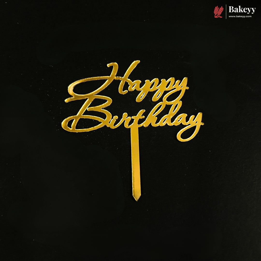 Gold metallic 'Happy Birthday' script cake topper on a black background, with a small Bakeyy logo in the top right corner.