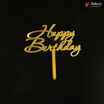 Gold metallic 'Happy Birthday' script cake topper on a black background, with a small Bakeyy logo in the top right corner.