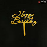 Gold metallic 'Happy Birthday' script cake topper on a black background, with a small Bakeyy logo in the top right corner.