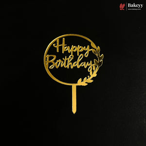 A gold metal 'Happy Birthday' cake topper with a laurel wreath design on a black background, featuring a Bakeyy brand watermark in the top right corner.