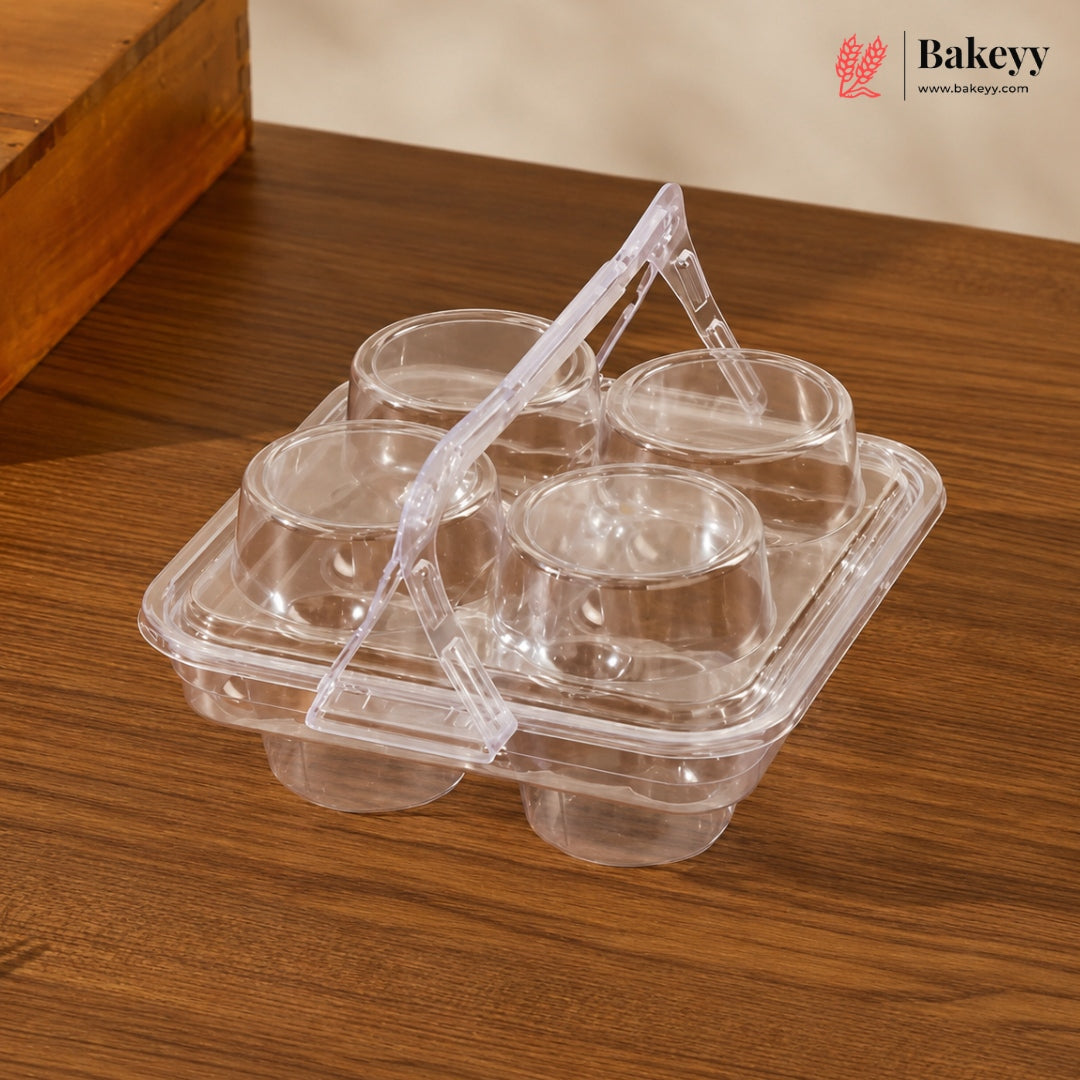 A clear plastic six-cup bakery tray with a built-in carrying handle, shown on a wooden tabletop. The Bakeyy brand logo is visible in the top right corner.