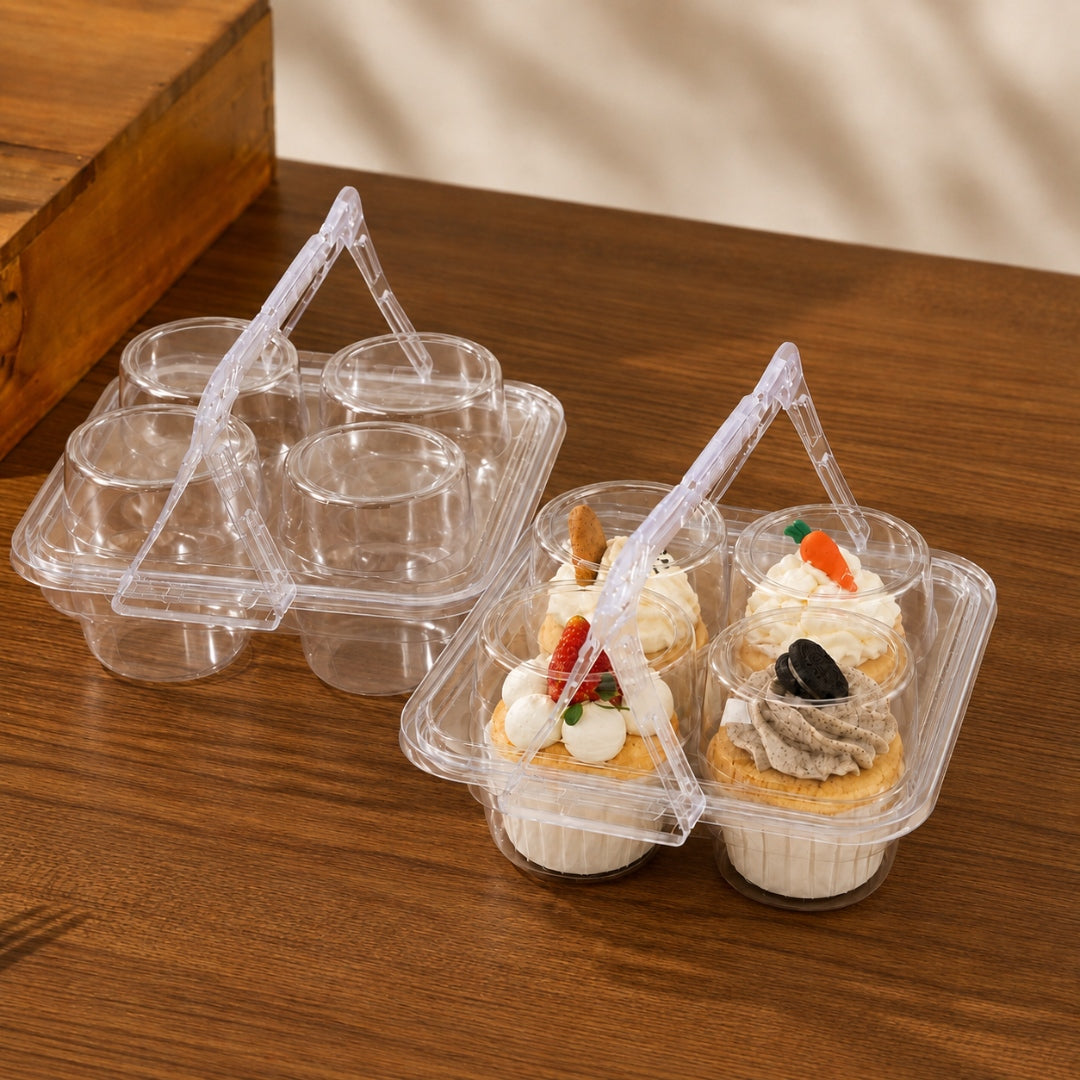 Two clear plastic cupcake carrier trays with triangular handles, one empty and one holding two decorated cupcakes, set on a wooden tabletop.