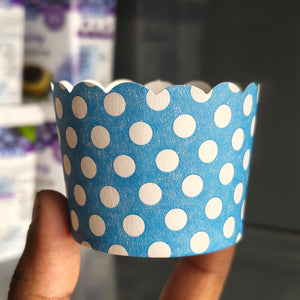 A hand holding a blue paper cupcake liner decorated with white polka dots, set against a blurred background.