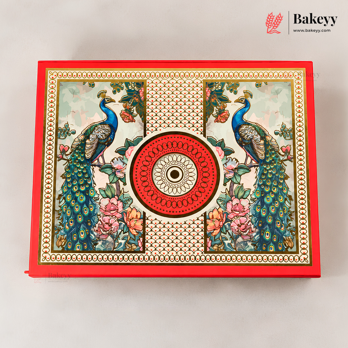 A decorative rectangular baking box with a red border and an ornate printed lid featuring two peacocks, floral motifs, and a central circular medallion. The Bakeyy logo appears in the top right corner.
