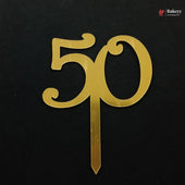 A gold metallic 50th birthday cake topper with a flat base stake, shown on a black background.