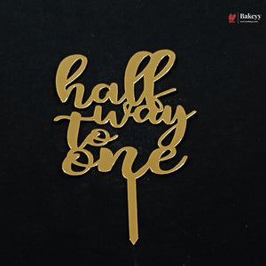 Gold acrylic cake topper with the phrase 'half way to one' in cursive script on a black background, with a Bakeey brand watermark in the top right corner.