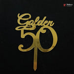 A gold metallic 'Golden 50' cake topper with a single wire stake, shown on a solid black background. A small 'Bakeyy' brand watermark is visible in the top right corner.