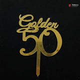 A gold metallic 'Golden 50' cake topper with a single wire stake, shown on a solid black background. A small 'Bakeyy' brand watermark is visible in the top right corner.